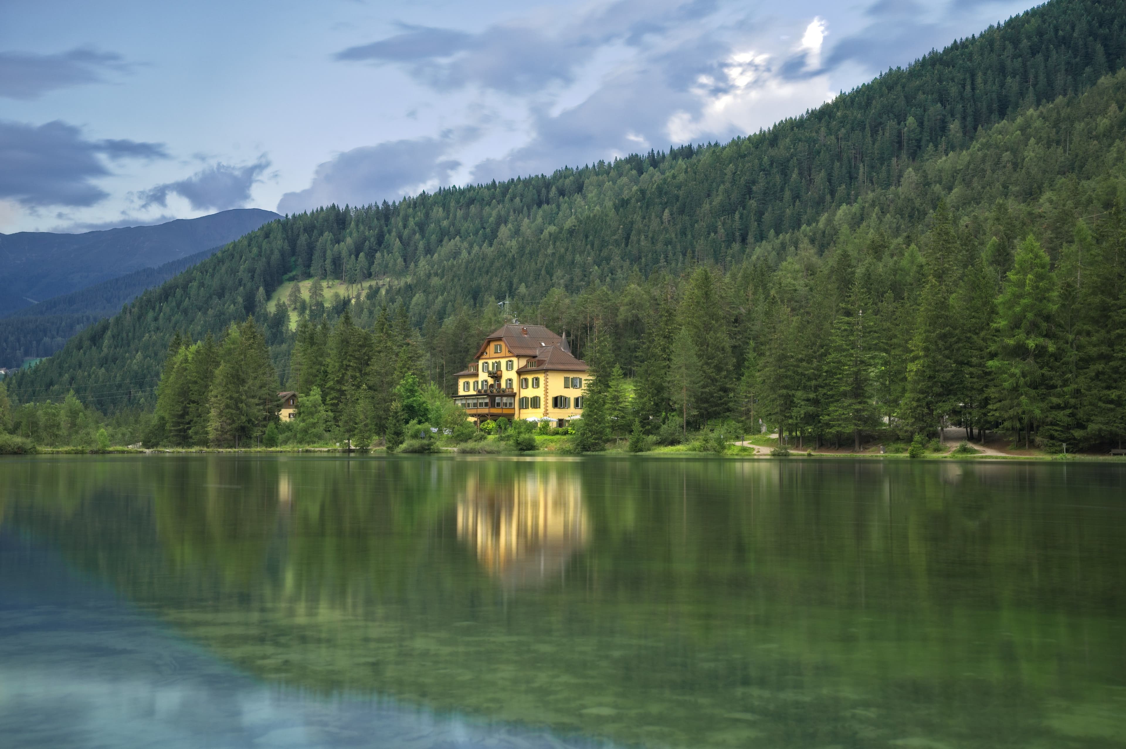 Une maison se reflète dans une eau calme sous une montagne boisée