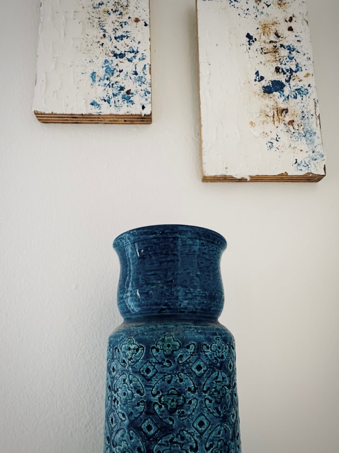 A blue ceramic vase beneath a framed artwork